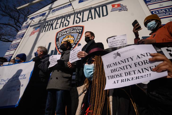 A handful of people protest outside of the Rikers Island sign in Queens with their own signs saying "humanity and dignity for detainees at Rikers."